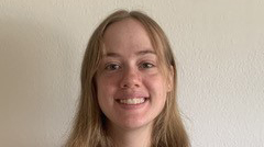 Portrait of a current Gannon Scholar with long light brown hair, smiling, standing in front of a plain light-colored wall.